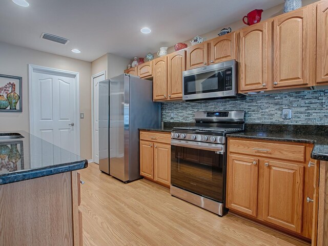 kitchen featuring appliances with stainless steel finishes, light wood-style flooring, decorative backsplash, dark stone countertops, and recessed lighting