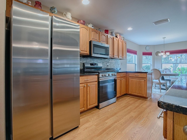 kitchen with tasteful backsplash, stainless steel appliances, hanging light fixtures, an inviting chandelier, and light hardwood / wood-style flooring