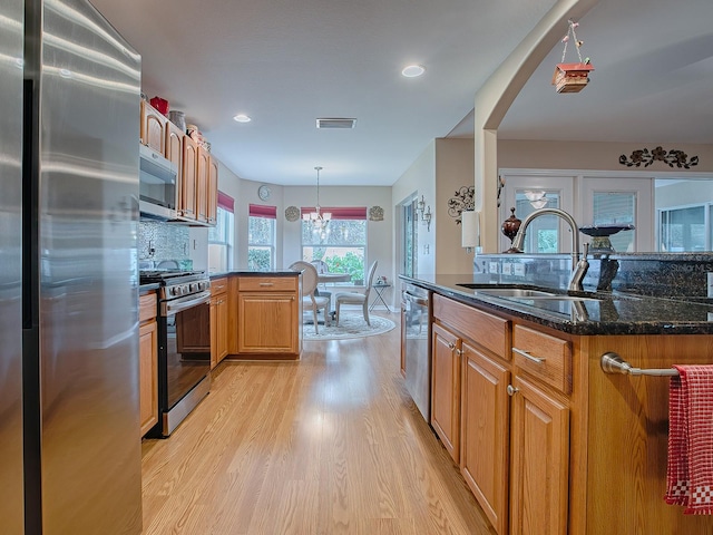 kitchen with dark stone counters, sink, light wood-type flooring, appliances with stainless steel finishes, and decorative light fixtures