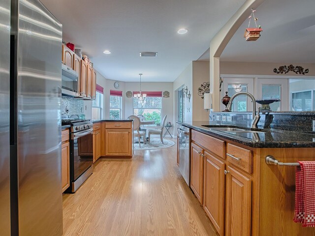 kitchen with stainless steel appliances, a sink, light wood-type flooring, dark stone countertops, and decorative light fixtures