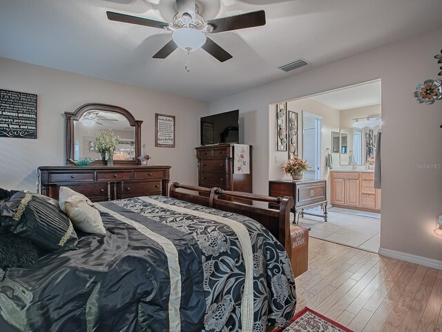 bedroom with light wood finished floors, a ceiling fan, ensuite bath, baseboards, and a sink