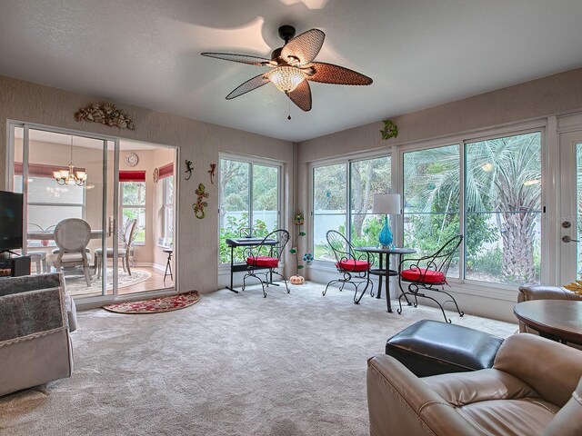 living area featuring healthy amount of natural light, carpet flooring, ceiling fan, and a chandelier
