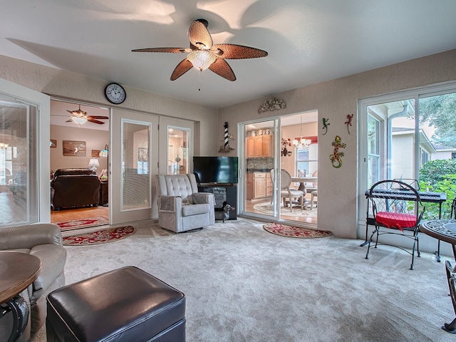 carpeted living room with ceiling fan with notable chandelier