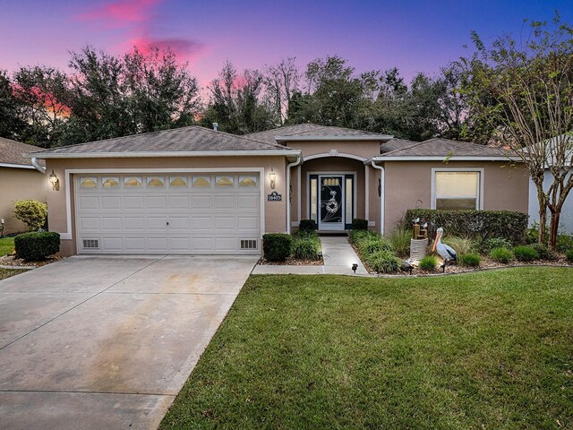 ranch-style home featuring a garage, driveway, stucco siding, and a front lawn