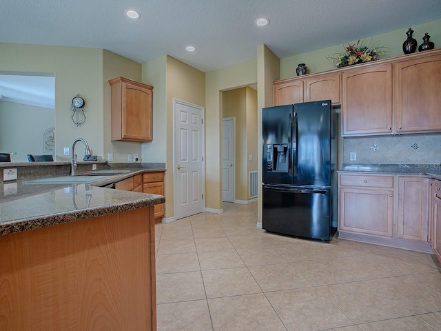 kitchen featuring black fridge, light tile patterned floors, sink, backsplash, and dark stone countertops