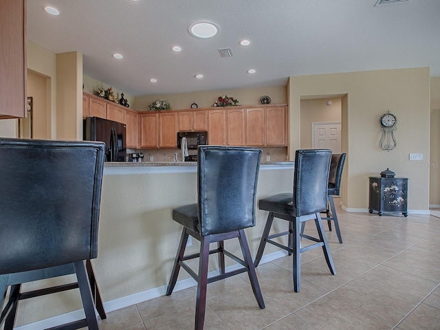 kitchen with black appliances, light tile patterned floors, decorative backsplash, a breakfast bar, and kitchen peninsula