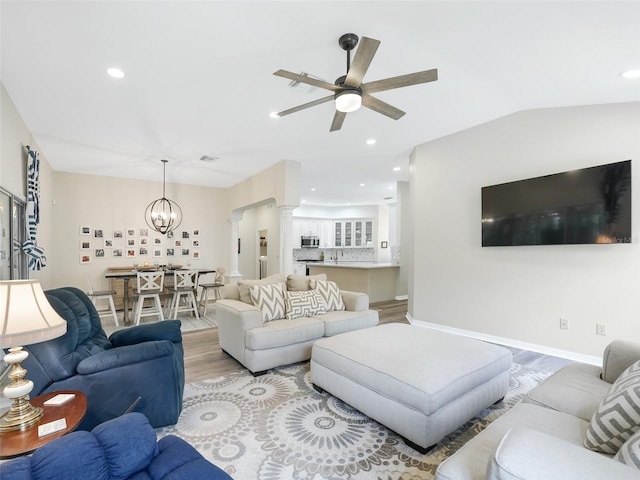 living room with ceiling fan with notable chandelier, light hardwood / wood-style flooring, lofted ceiling, and decorative columns