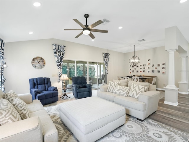 living room featuring lofted ceiling, hardwood / wood-style flooring, ornate columns, and ceiling fan with notable chandelier