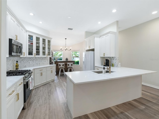 kitchen with stainless steel appliances, light wood-type flooring, decorative light fixtures, sink, and kitchen peninsula