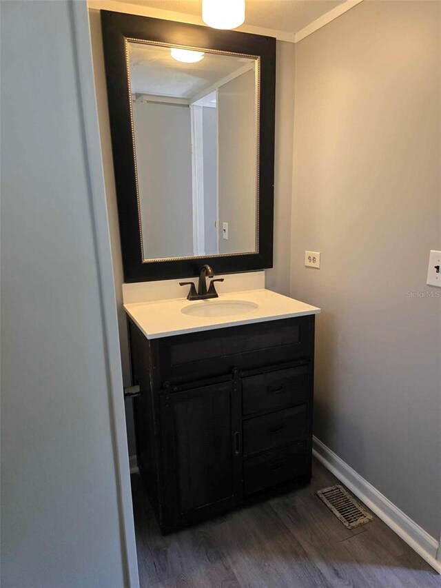 bathroom with wood finished floors, vanity, visible vents, baseboards, and ornamental molding