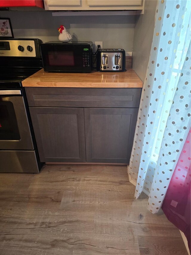 kitchen with black microwave, stainless steel range with electric stovetop, and light wood-style floors