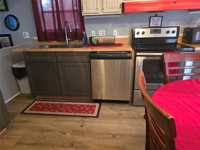 kitchen featuring appliances with stainless steel finishes, ventilation hood, light wood-type flooring, wooden counters, and a sink