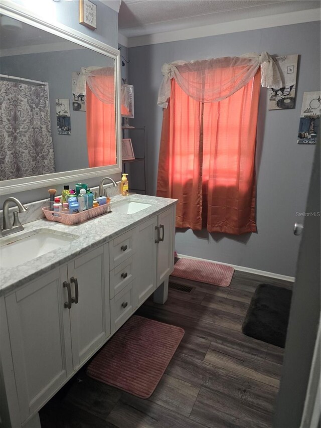 full bath featuring double vanity, wood finished floors, a sink, and crown molding