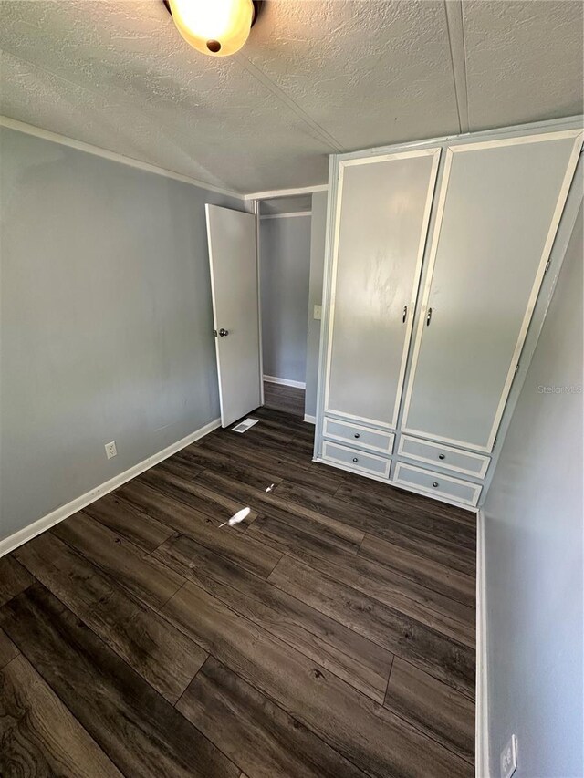 unfurnished bedroom featuring dark wood-style floors, a closet, a textured ceiling, and baseboards