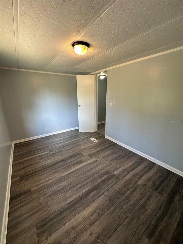 empty room with visible vents, a textured ceiling, baseboards, and dark wood-type flooring