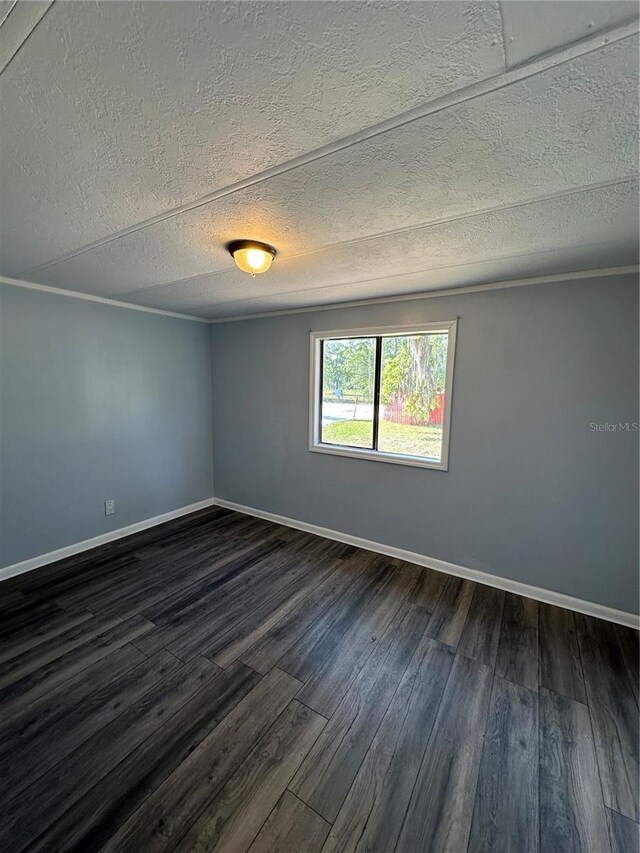 empty room with dark wood-style floors, baseboards, a textured ceiling, and ornamental molding