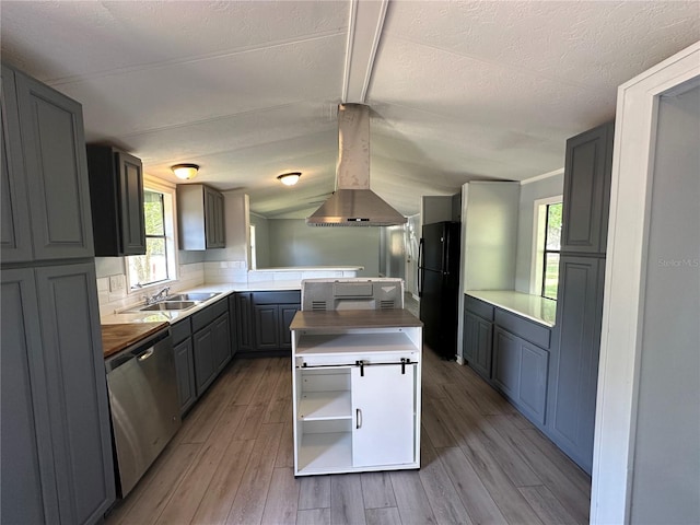 kitchen featuring dishwasher, butcher block countertops, freestanding refrigerator, island exhaust hood, and a sink