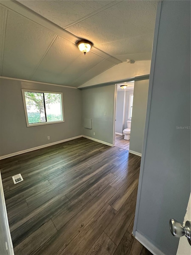 unfurnished room with lofted ceiling, a textured ceiling, visible vents, baseboards, and dark wood-style floors