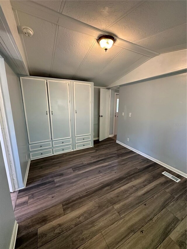 unfurnished bedroom with lofted ceiling with beams, baseboards, visible vents, and dark wood-type flooring