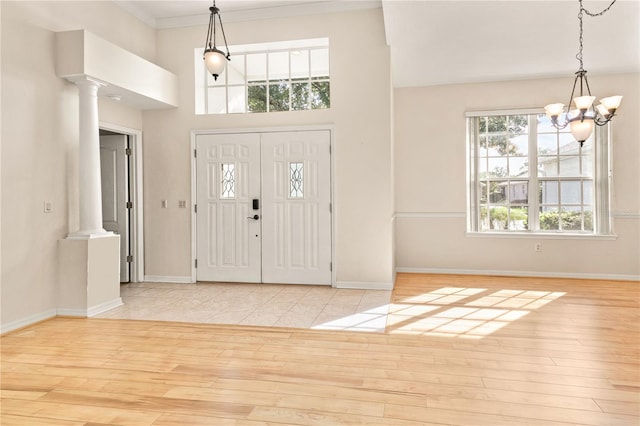 entrance foyer featuring ornamental molding, ornate columns, a wealth of natural light, and light hardwood / wood-style floors