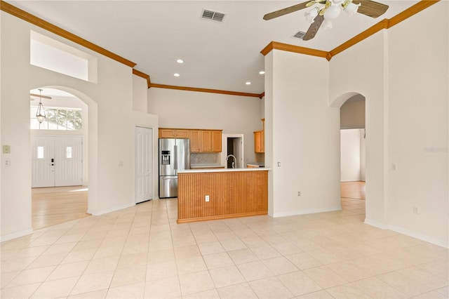 kitchen with crown molding, a towering ceiling, stainless steel refrigerator with ice dispenser, sink, and kitchen peninsula