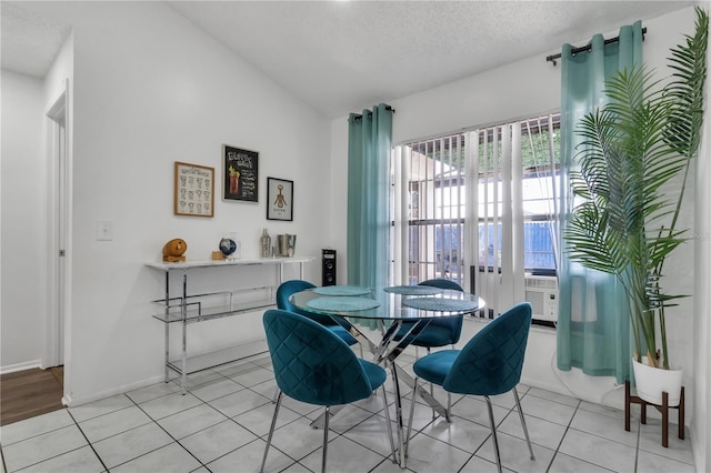 dining space with a textured ceiling, light tile patterned floors, lofted ceiling, and cooling unit