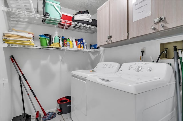 clothes washing area featuring light tile patterned flooring, a textured ceiling, cabinets, and washer and dryer