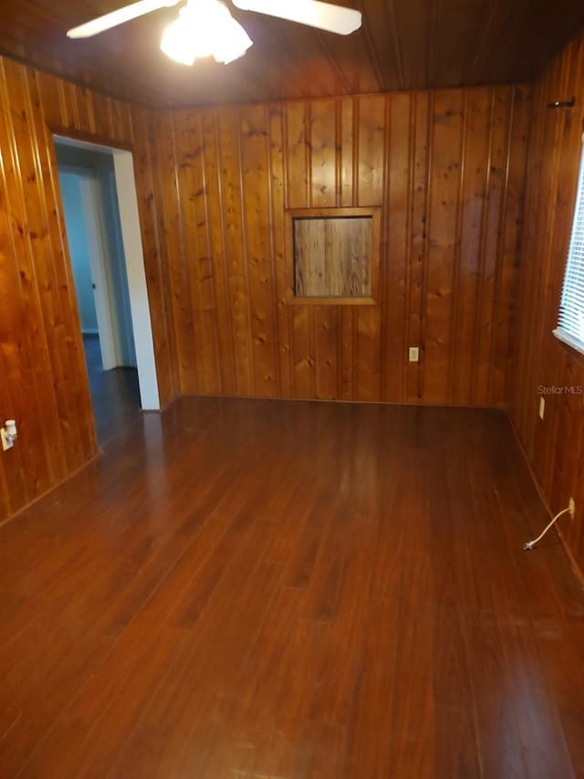 spare room with ceiling fan, wooden walls, and dark hardwood / wood-style flooring