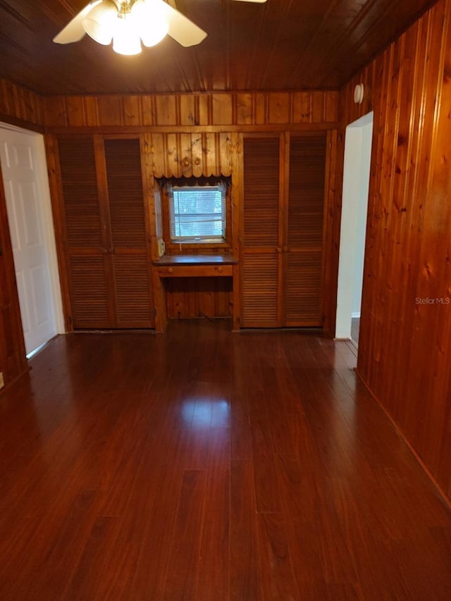 unfurnished living room with wood walls, dark wood-type flooring, ceiling fan, and wood ceiling