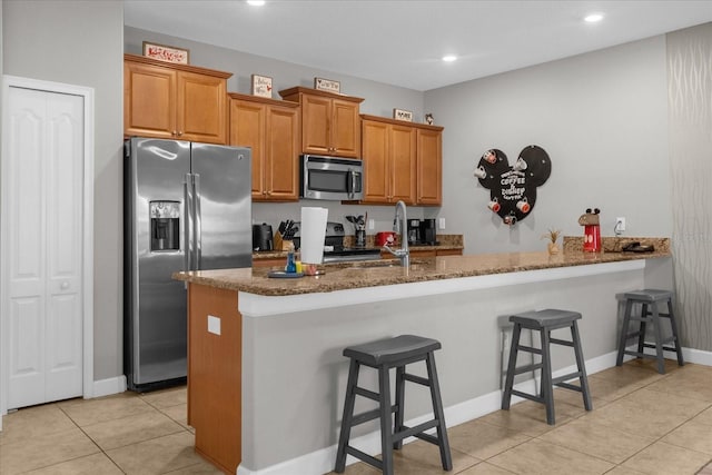 kitchen featuring stone countertops, a kitchen breakfast bar, a peninsula, stainless steel appliances, and a sink