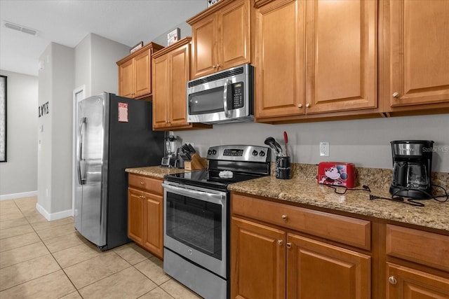 kitchen with light stone counters, light tile patterned floors, stainless steel appliances, visible vents, and brown cabinetry