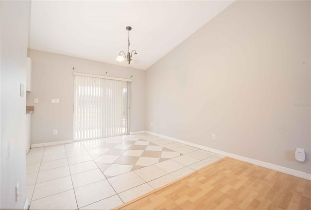 spare room with light wood-type flooring, vaulted ceiling, and a notable chandelier