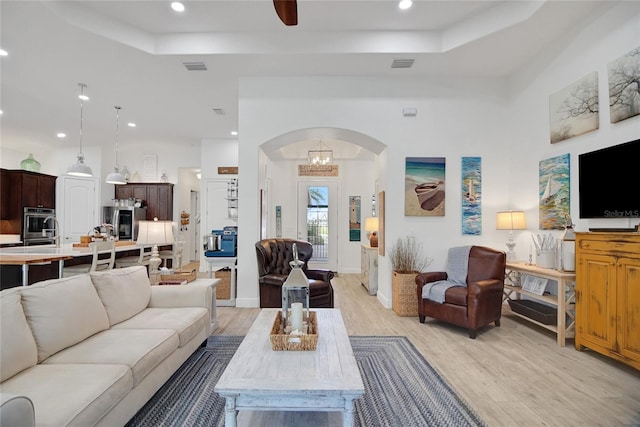 living room featuring ceiling fan with notable chandelier, a raised ceiling, and light hardwood / wood-style flooring