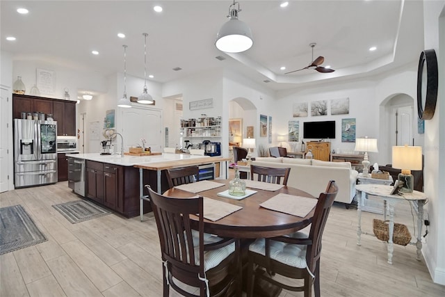 dining space featuring a tray ceiling, ceiling fan, sink, and light hardwood / wood-style floors