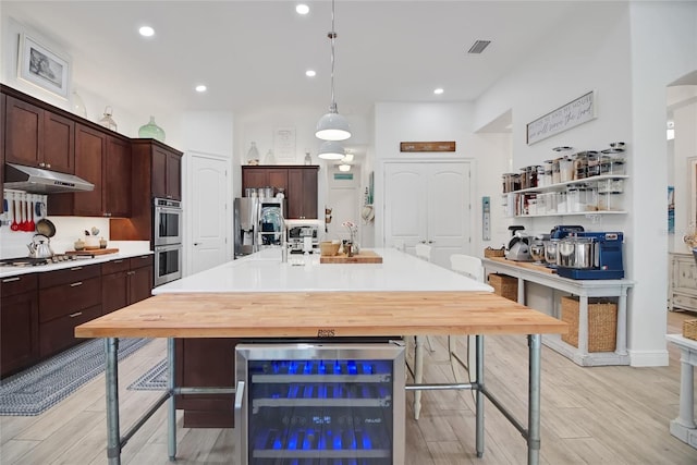 kitchen featuring light hardwood / wood-style flooring, appliances with stainless steel finishes, decorative light fixtures, a breakfast bar area, and beverage cooler