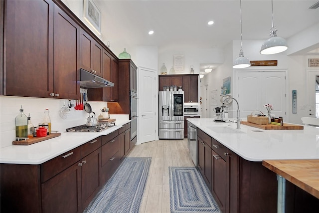 kitchen featuring backsplash, hanging light fixtures, sink, light hardwood / wood-style flooring, and appliances with stainless steel finishes