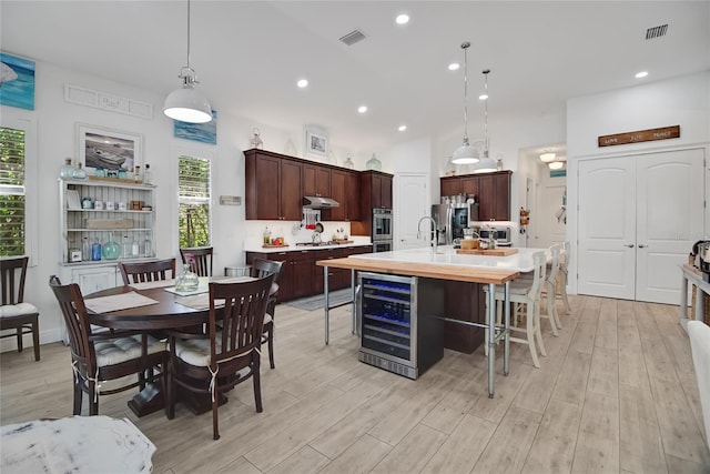 kitchen featuring hanging light fixtures, wine cooler, light hardwood / wood-style flooring, an island with sink, and stainless steel appliances