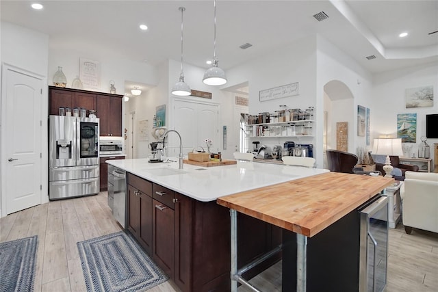 kitchen with appliances with stainless steel finishes, decorative light fixtures, beverage cooler, and a kitchen island with sink