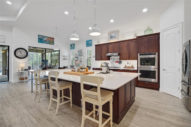 kitchen featuring hanging light fixtures, an island with sink, a kitchen bar, appliances with stainless steel finishes, and light wood-type flooring