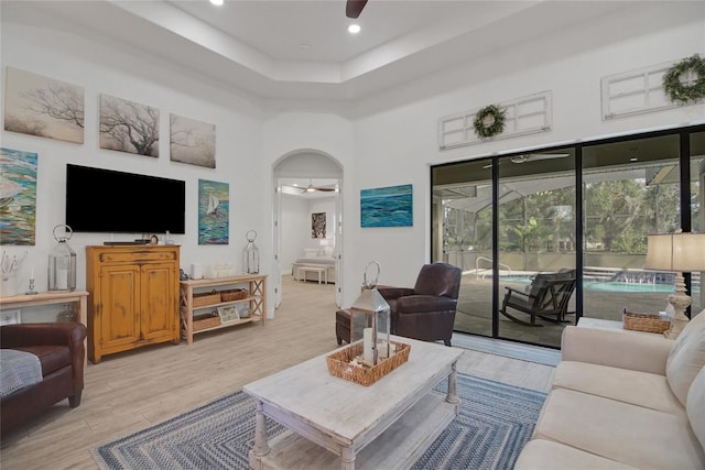 living room with a towering ceiling, a tray ceiling, light hardwood / wood-style flooring, and ceiling fan