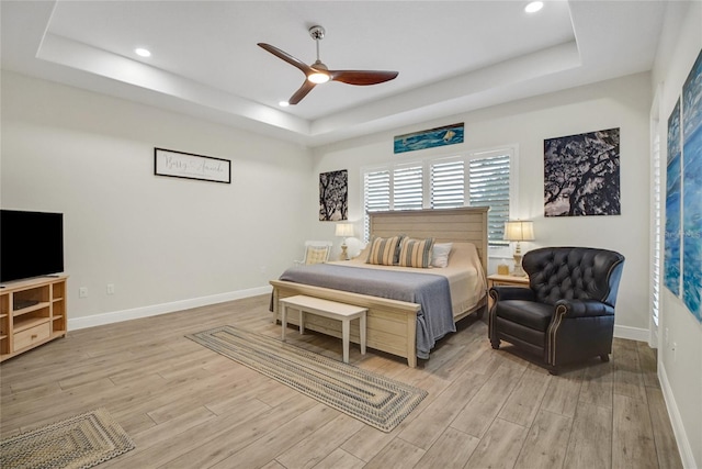 bedroom with a raised ceiling, ceiling fan, and light hardwood / wood-style floors