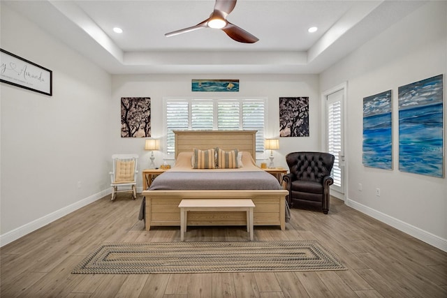 bedroom featuring a tray ceiling, ceiling fan, and light wood-type flooring