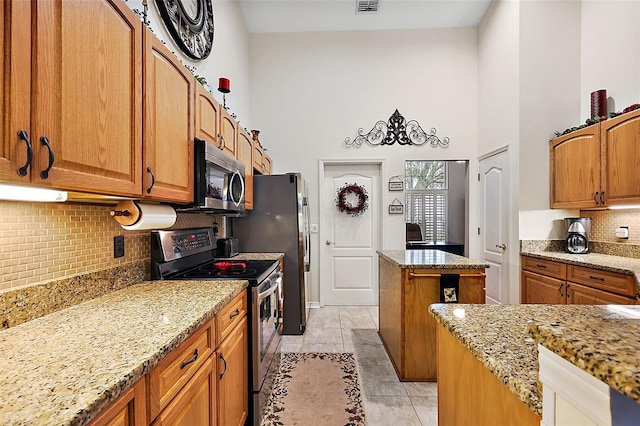 kitchen featuring a towering ceiling, light tile patterned flooring, a kitchen island, light stone countertops, and appliances with stainless steel finishes