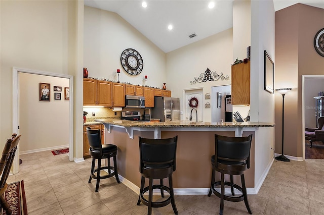 kitchen featuring stainless steel appliances, light stone counters, kitchen peninsula, a kitchen breakfast bar, and high vaulted ceiling