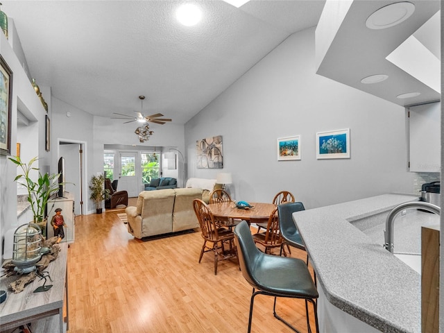 dining space featuring high vaulted ceiling, wood-type flooring, ceiling fan, and a textured ceiling