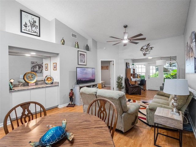 dining space with high vaulted ceiling, ceiling fan, a textured ceiling, and light hardwood / wood-style floors