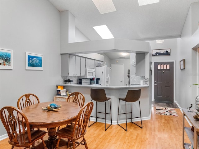 dining area featuring a textured ceiling, light hardwood / wood-style flooring, and high vaulted ceiling