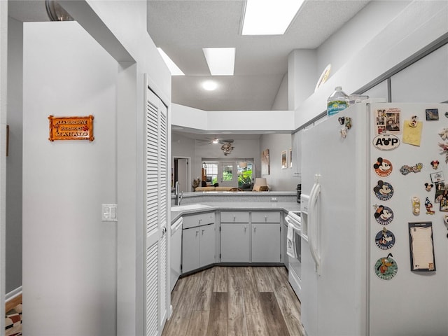 kitchen with a textured ceiling, white appliances, sink, hardwood / wood-style floors, and kitchen peninsula