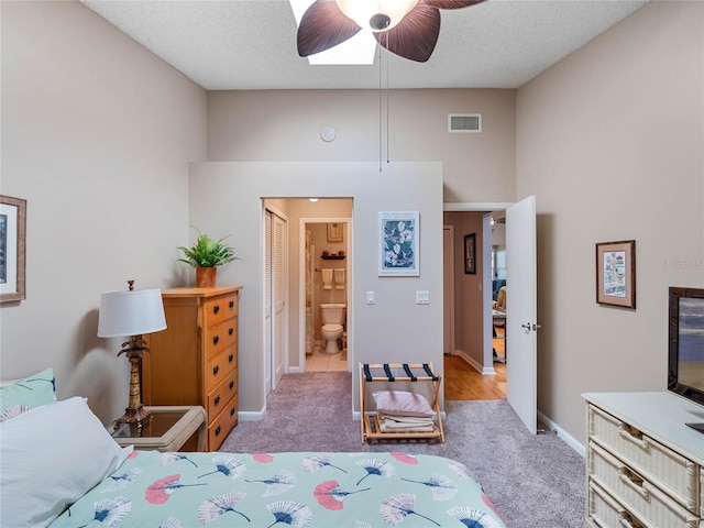 bedroom featuring a textured ceiling, light colored carpet, ceiling fan, and connected bathroom