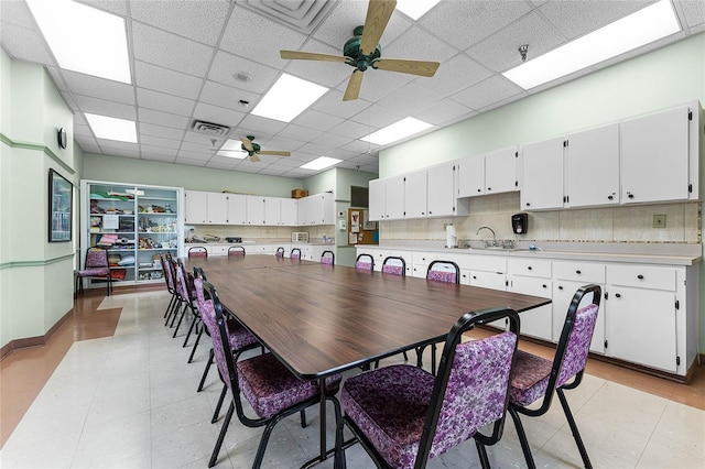 dining space with ceiling fan, sink, and a drop ceiling